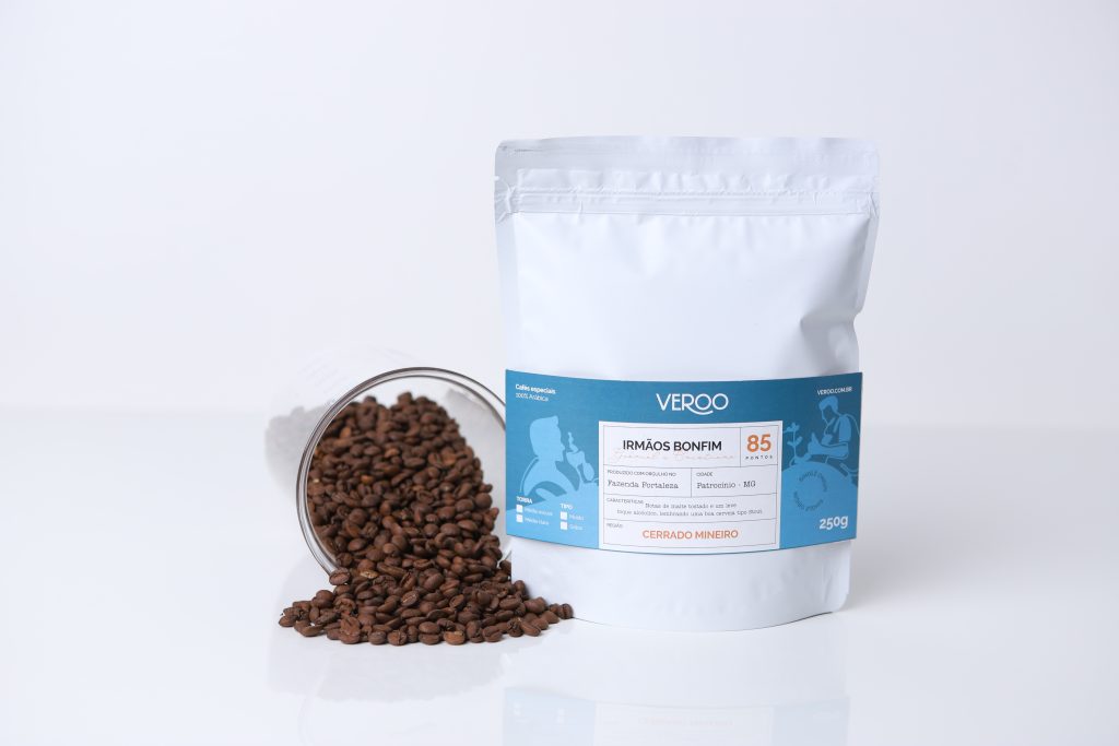 Foto da embalagem do café dos irmãos Bonfim e grãos caídos em uma superfície lisa ao lado da embalagem