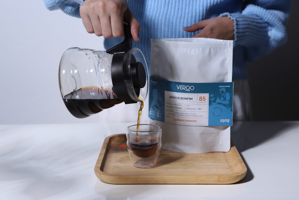 Foto do café dos irmãos Bonfim sendo derramado em um copo e ao lado uma embalagem do café