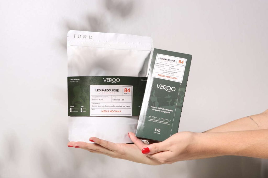 Mão segurando as embalagens de café especial do Eduardo da edição de junho do Clube Veroo