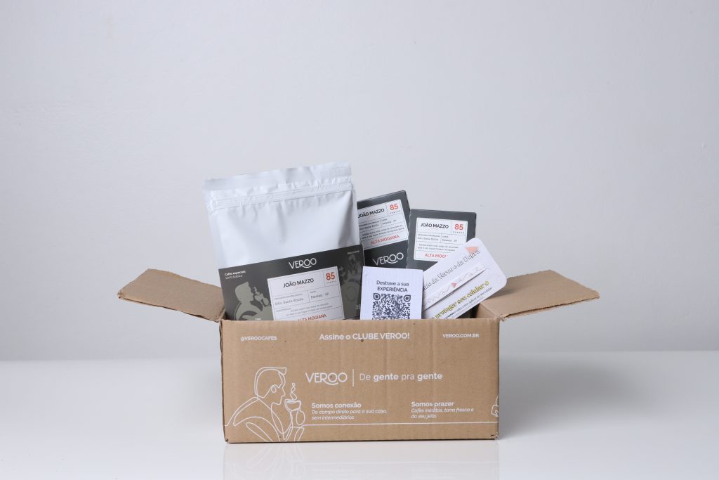 Imagem da box do mês de agosto (café em capsulas, café moído e uma faixa de colar no celular da Dobra - mimo do mês)